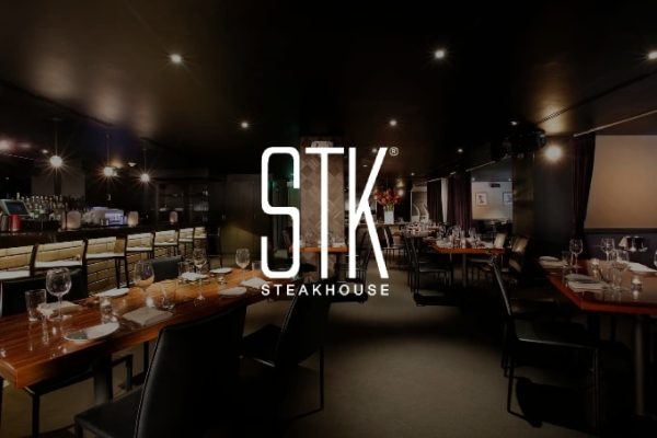 A dimly lit restaurant interior with set tables, a bar, and "STK STEAKHOUSE" in white overlay.